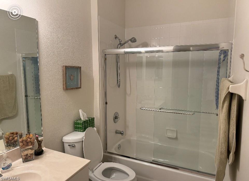 Full bathroom featuring enclosed tub / shower combo, vanity, and a textured wall