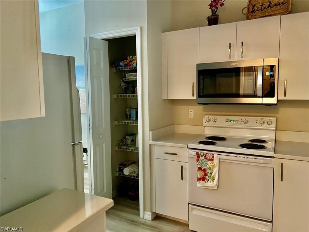 Kitchen featuring white appliances, light countertops, white cabinets, and light wood finished floors
