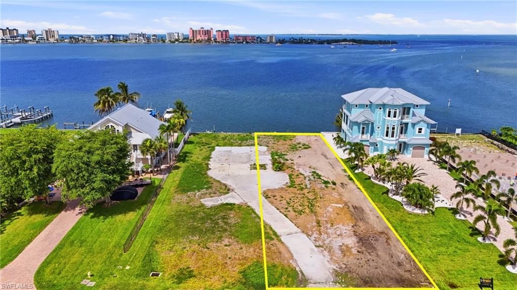 Waterfront lot with established concrete driveway, bordered by green landscaping and mature palm trees- Virtually Edited Image
