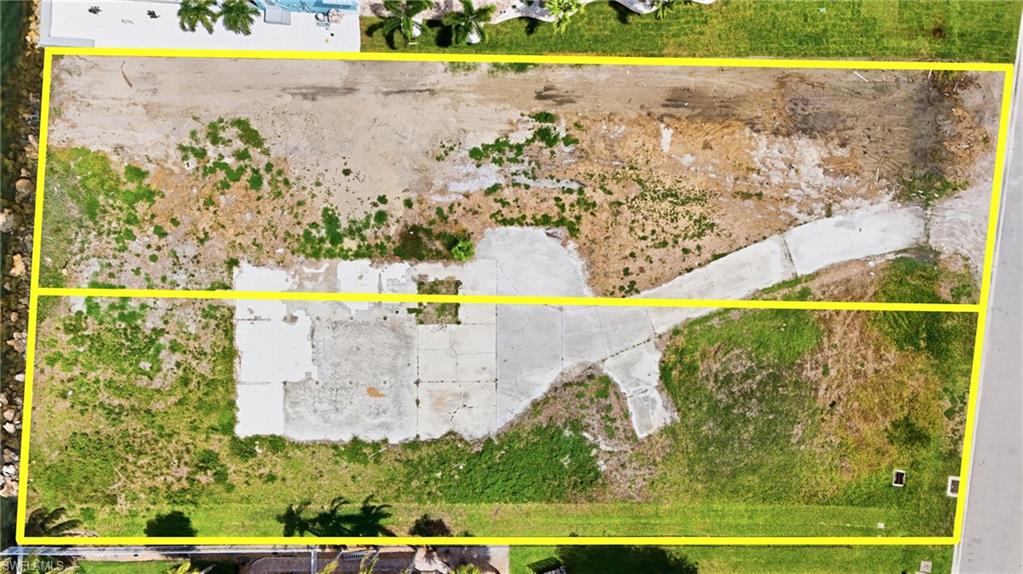 Expansive aerial view of a vacant lot with a concrete driveway and existing concrete pads- Virtually Edited Image