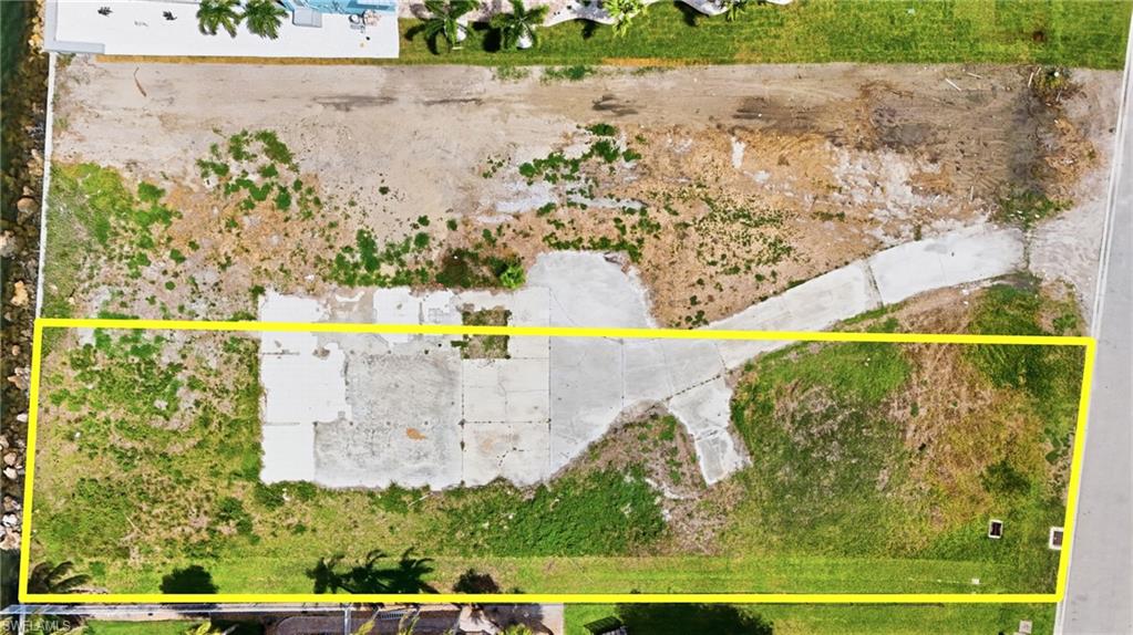 Expansive cleared lot outlined with a yellow boundary, featuring concrete pads and a visible driveway - Virtually Edited Image