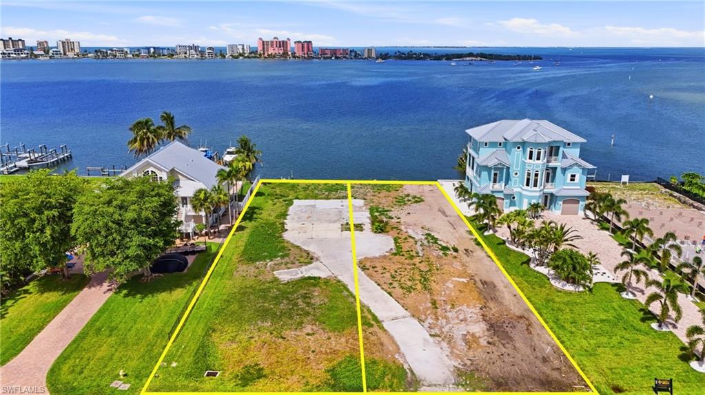 Expansive waterfront land parcel featuring a direct water frontage, concrete drive, and surrounding mature landscaping - Virtually Edited Image