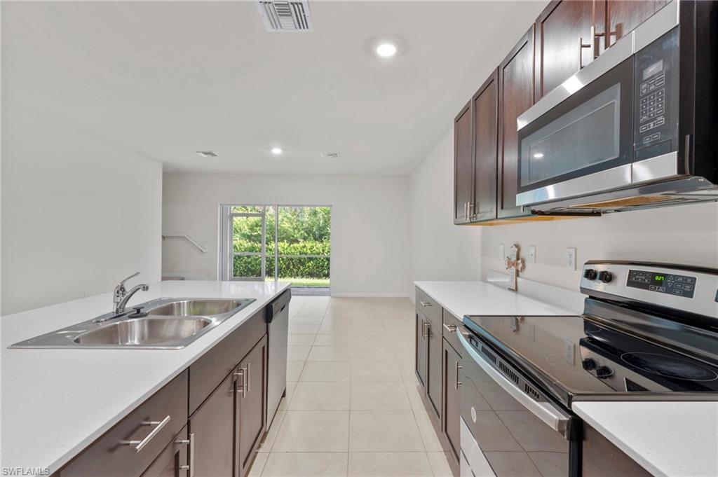 Kitchen with stainless steel appliances, dark brown cabinetry, recessed lighting, and light tile patterned flooring