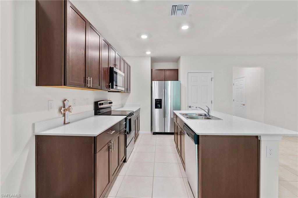 Kitchen featuring appliances with stainless steel finishes, dark brown cabinets, light tile patterned floors, recessed lighting, and a kitchen island with sink