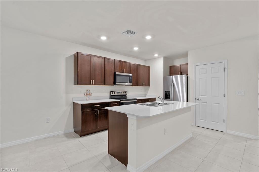 Kitchen featuring stainless steel appliances, light countertops, a kitchen island with sink, dark brown cabinets, and light tile patterned floors