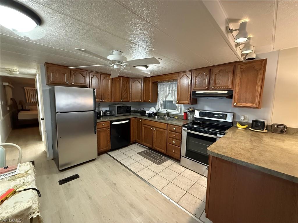 Kitchen with stainless steel appliances, brown cabinets, light wood-style floors, under cabinet range hood, and a textured ceiling