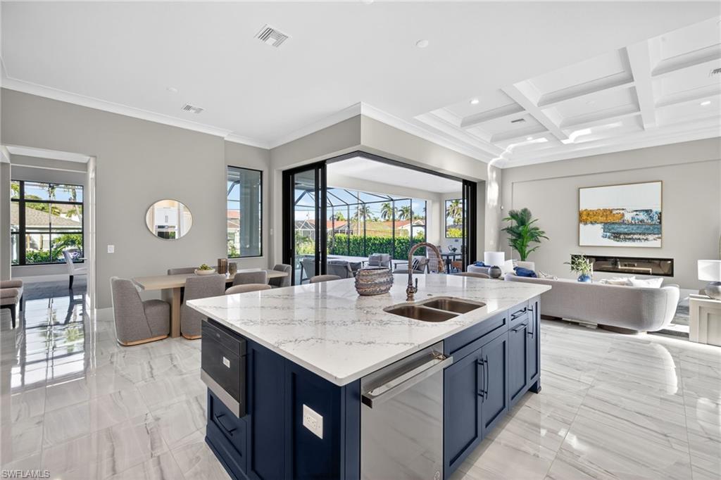 Kitchen featuring open floor plan, light stone countertops, blue cabinets, dishwasher, and a kitchen island with sink