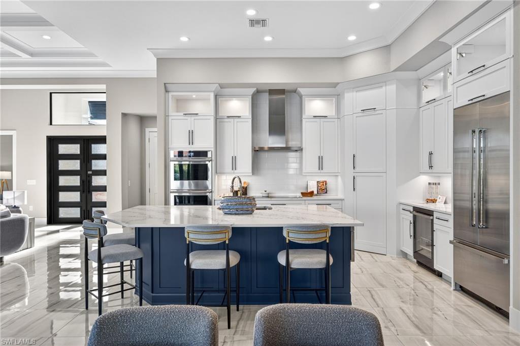Kitchen with blue cabinets, a kitchen breakfast bar, light stone countertops, glass insert cabinets, and an island with sink