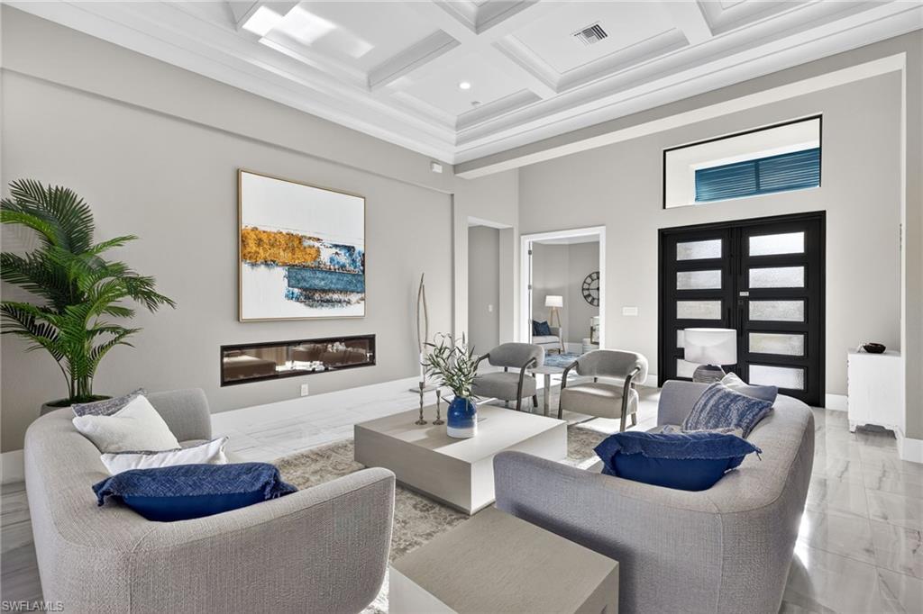 Living room with a high ceiling, coffered ceiling, beam ceiling, marble tiled flooring, and a glass covered fireplace