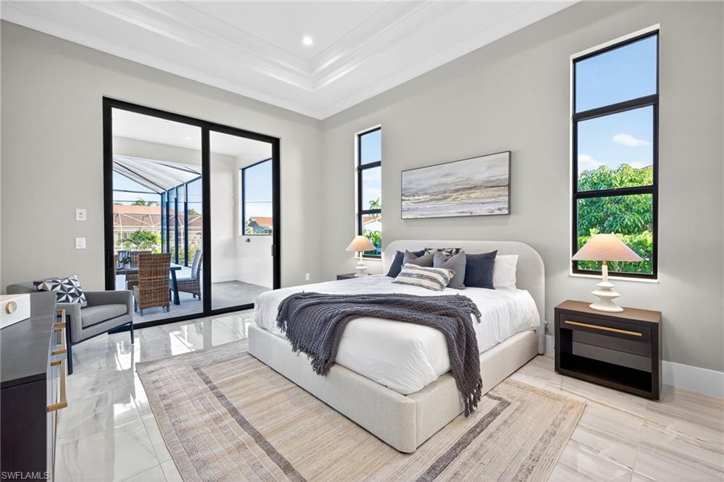 Bedroom featuring a tray ceiling, multiple windows, access to exterior, ornamental molding, and light marble finish floors
