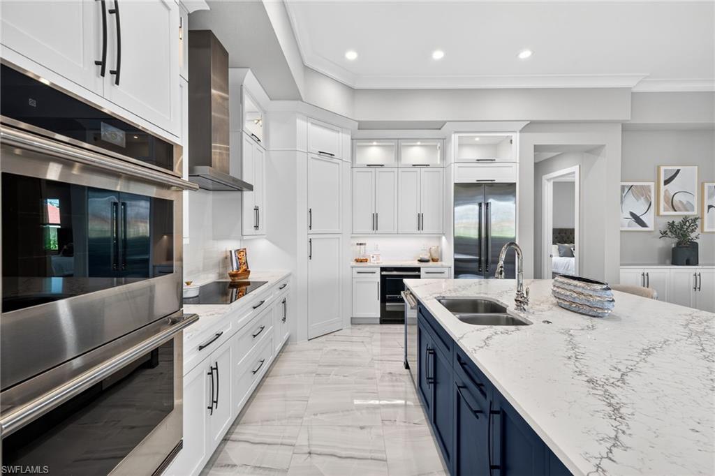 Kitchen featuring stainless steel appliances, white cabinets, light stone counters, wall chimney exhaust hood, and glass insert cabinets