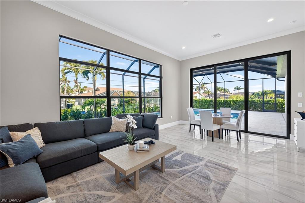 Living area featuring a sunroom, light marble finish flooring, crown molding, healthy amount of natural light, and recessed lighting