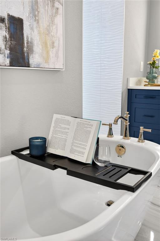 Bathroom view of a tub, a textured wall, and vanity
