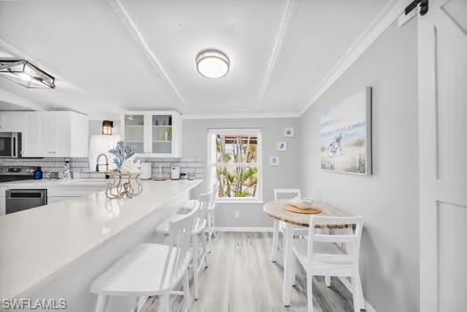 Kitchen featuring backsplash, a kitchen breakfast bar, white cabinets, light wood-type flooring, and crown molding