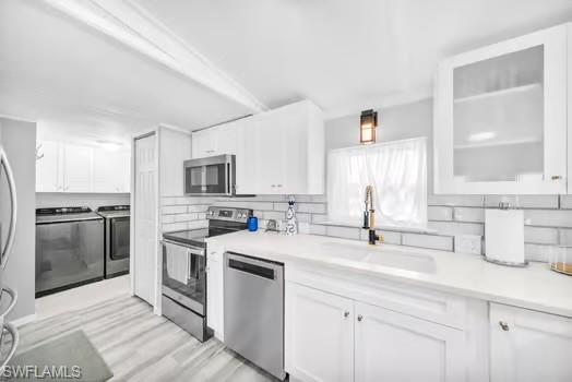 Kitchen with appliances with stainless steel finishes, white cabinetry, light countertops, washer and clothes dryer, and light wood-type flooring