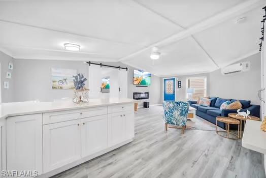 Living area with a barn door, vaulted ceiling, light wood-style flooring, and a wall mounted AC