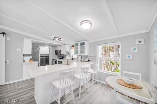 Kitchen with a barn door, white cabinetry, a kitchen bar, light countertops, and stainless steel appliances