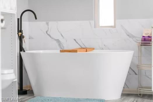 Full bathroom with tile walls, a soaking tub, and a wainscoted wall