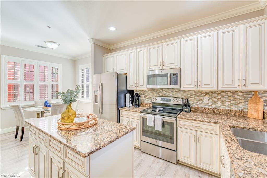 Kitchen featuring cream cabinets, stainless steel appliances, backsplash, ornamental molding, and light wood-style floors