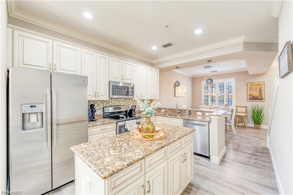 Kitchen with stainless steel appliances, backsplash, crown molding, light stone countertops, and light wood-style floors
