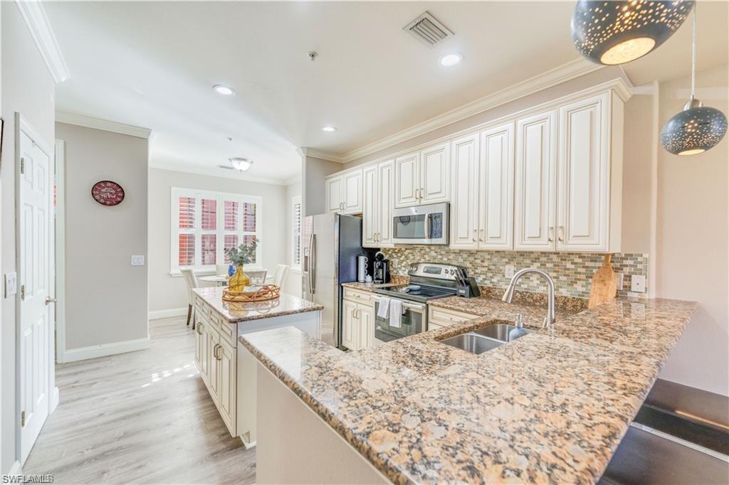 Kitchen featuring a center island, appliances with stainless steel finishes, decorative backsplash, ornamental molding, and light stone countertops