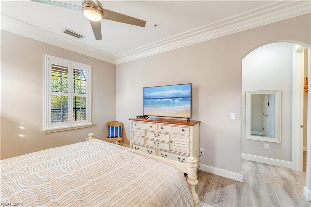 Bedroom with crown molding, light wood-style floors, a ceiling fan, and arched walkways