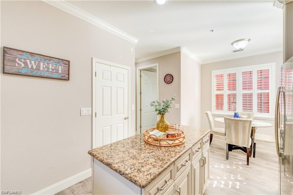 Kitchen with light stone counters, ornamental molding, a kitchen island, freestanding refrigerator, and cream cabinetry