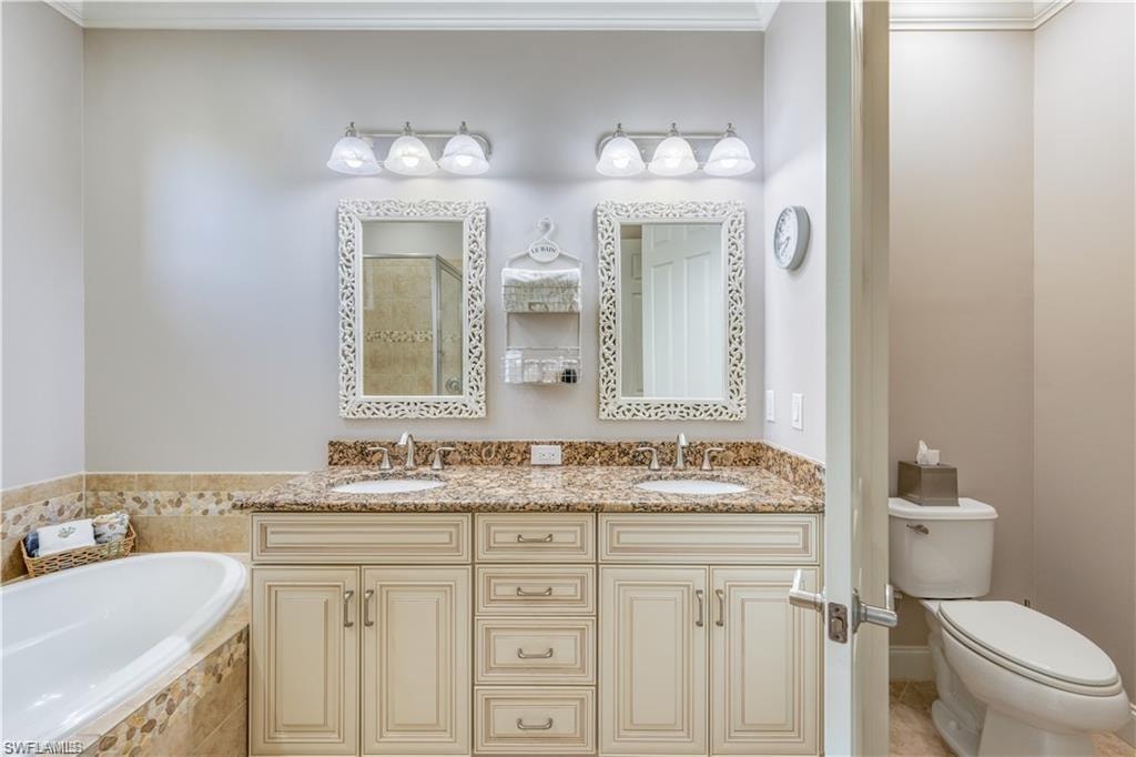 Bathroom featuring ornamental molding, a garden tub, double vanity, and a tile shower