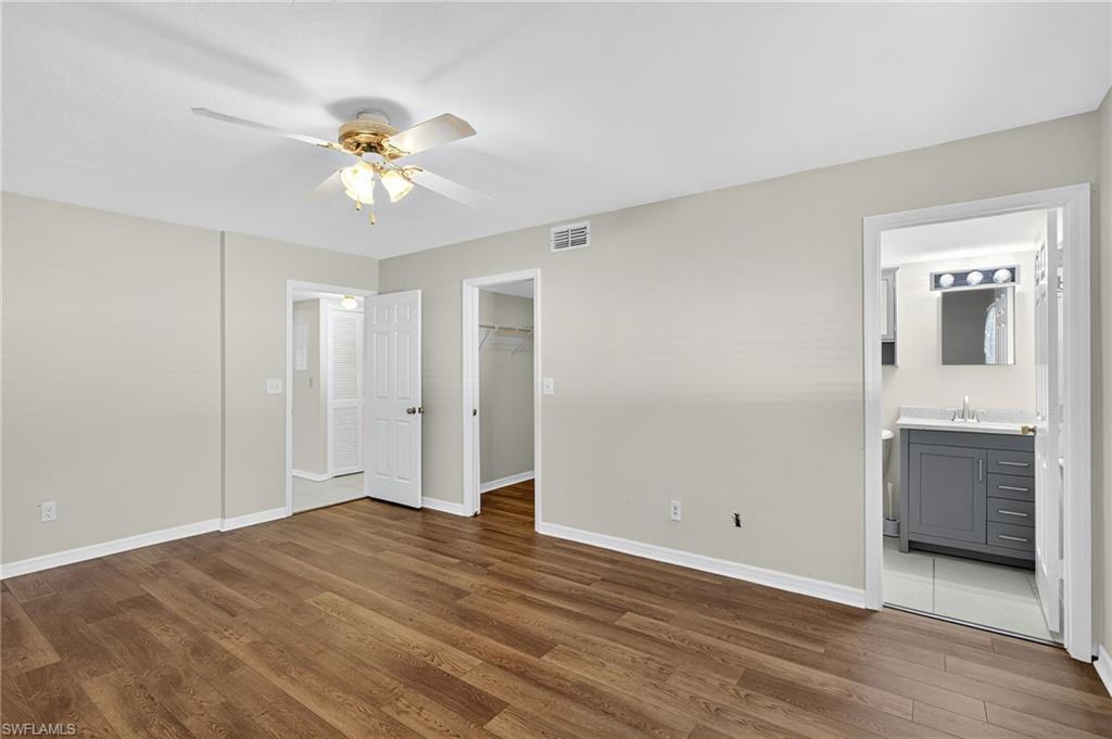 Unfurnished bedroom featuring wood finished floors, a spacious closet, a ceiling fan, and ensuite bathroom