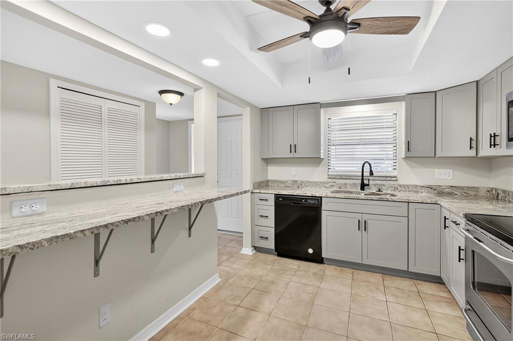 Kitchen with gray cabinets, a tray ceiling, electric stove, light stone counters, and recessed lighting