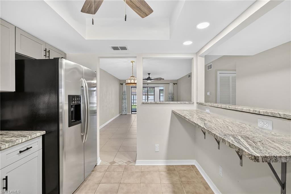 Kitchen featuring light stone countertops, a ceiling fan, stainless steel fridge, light tile patterned floors, and a raised ceiling