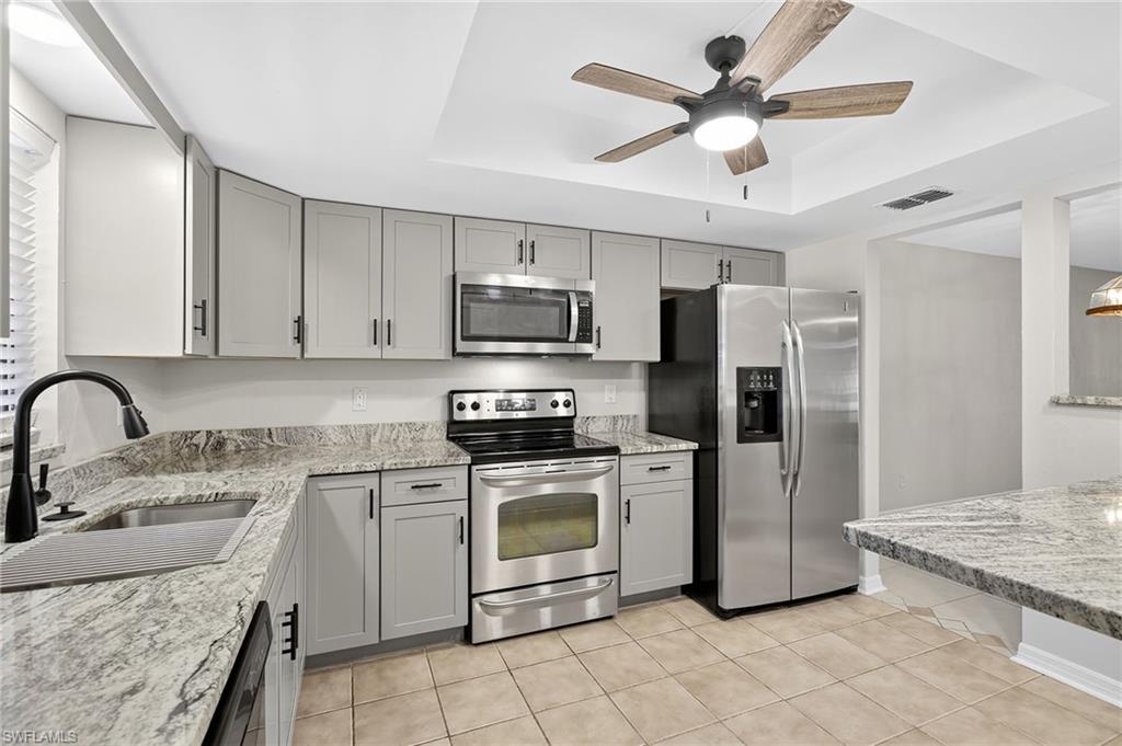 Kitchen with gray cabinets, a raised ceiling, stainless steel appliances, and light stone counters