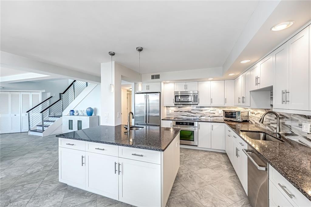 Kitchen featuring white cabinets, dark stone countertops, stainless steel appliances, backsplash, and hanging light fixtures