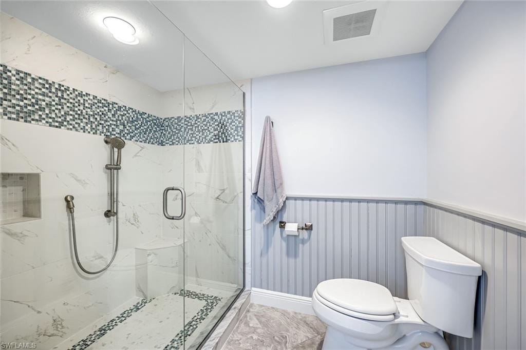 Bathroom with a marble finish shower, a wainscoted wall, and recessed lighting