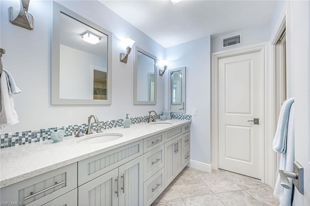 Full bathroom with double vanity, decorative backsplash, and light tile patterned floors