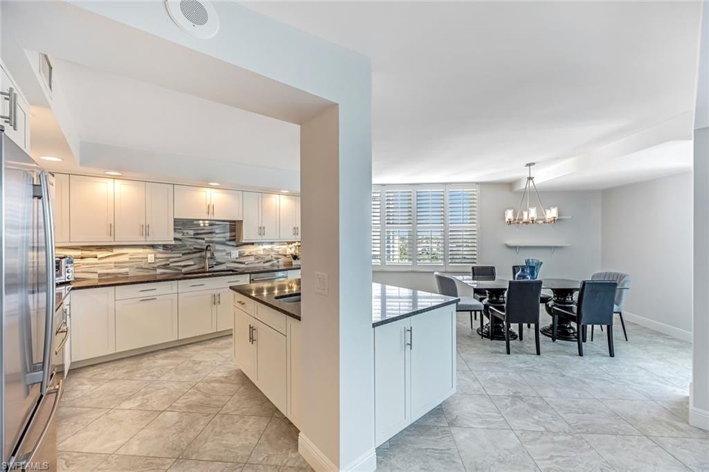 Kitchen with white cabinetry, stainless steel fridge, decorative backsplash, pendant lighting, and dark stone counters