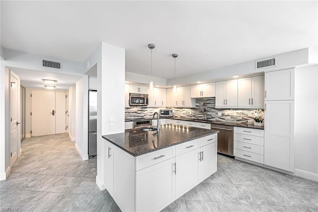 Kitchen with dark stone countertops, decorative light fixtures, stainless steel appliances, decorative backsplash, and white cabinets
