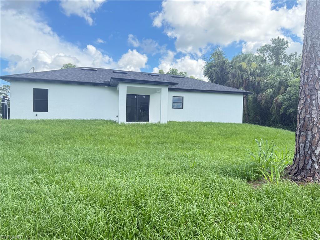 Back of house with a yard, stucco siding, and roof with shingles