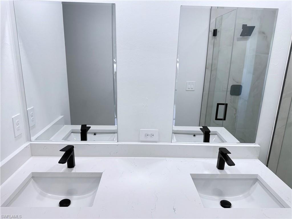 Full bath featuring a marble finish shower and double vanity