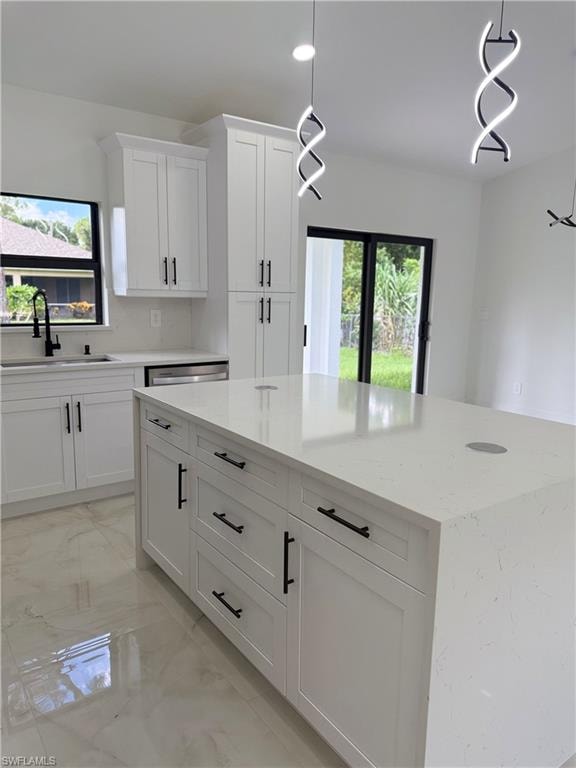 Kitchen with light marble finish flooring, pendant lighting, white cabinets, light stone countertops, and a center island