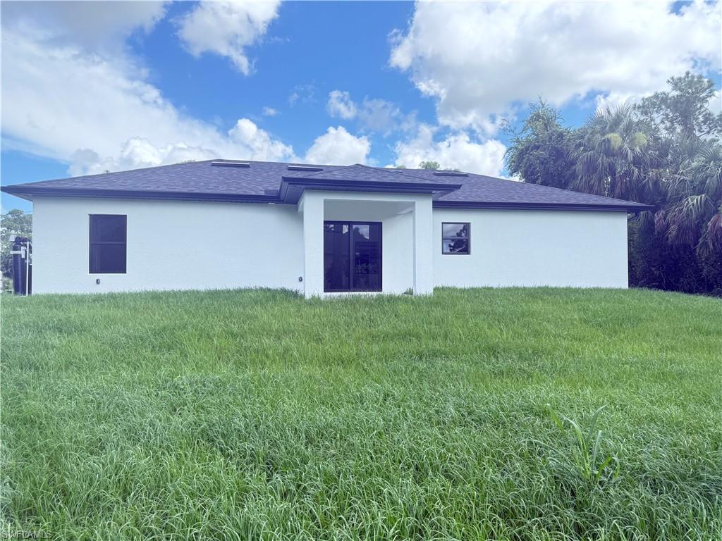 Rear view of property featuring stucco siding, a lawn, and a shingled roof