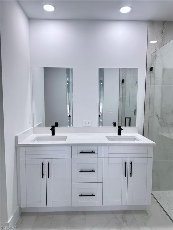 Bathroom featuring a marble finish shower, double vanity, light marble finish floors, and recessed lighting