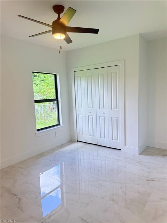 Unfurnished bedroom featuring light marble finish floors, a ceiling fan, and a closet