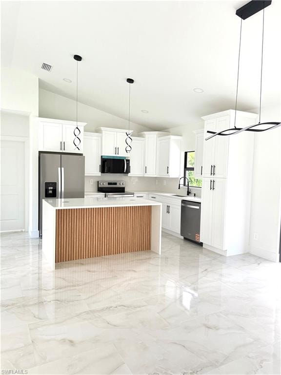 Kitchen featuring a kitchen island, white cabinets, light marble finish flooring, lofted ceiling, and hanging light fixtures