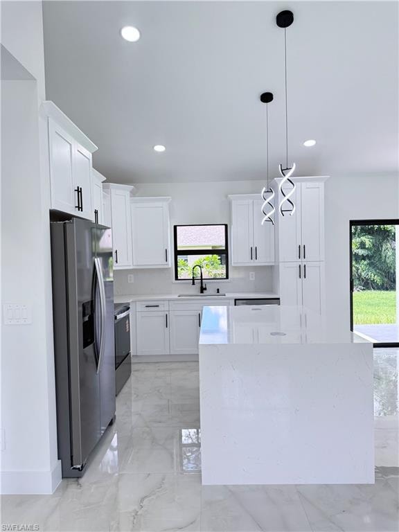 Kitchen featuring light marble finish flooring, appliances with stainless steel finishes, white cabinets, light stone counters, and pendant lighting