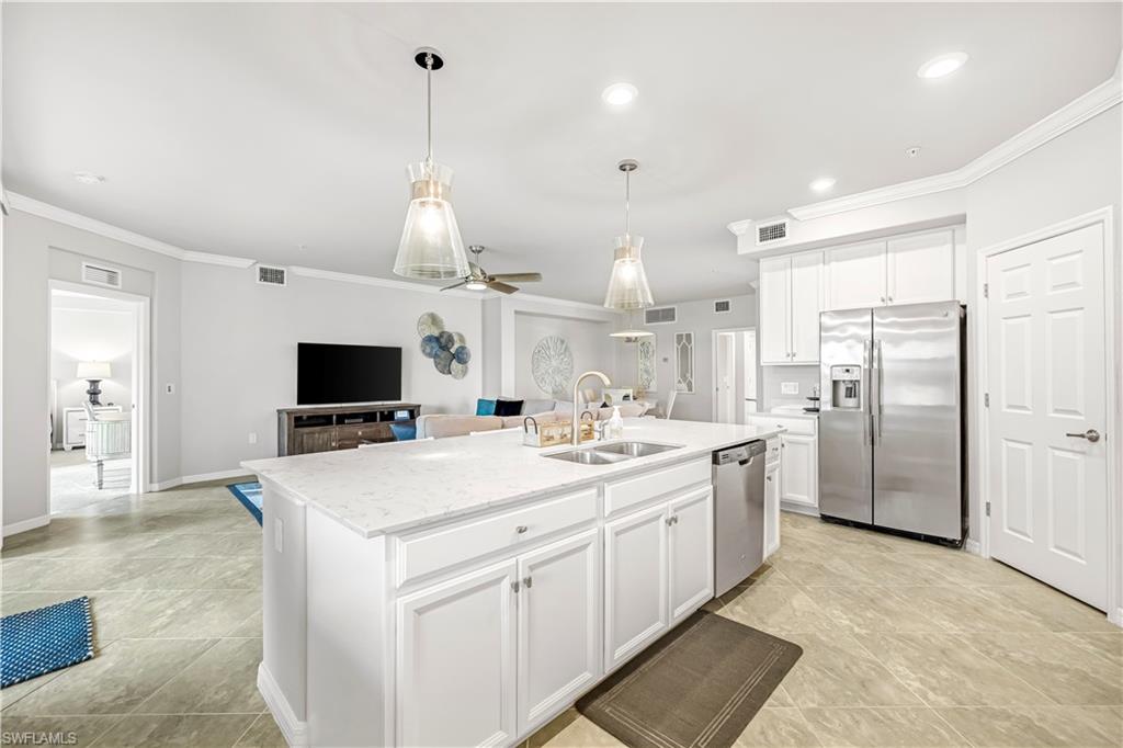 Kitchen featuring stainless steel appliances, hanging light fixtures, white cabinetry, ornamental molding, and open floor plan