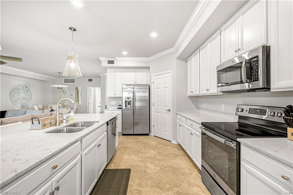 Kitchen with appliances with stainless steel finishes, decorative light fixtures, ornamental molding, white cabinets, and open floor plan