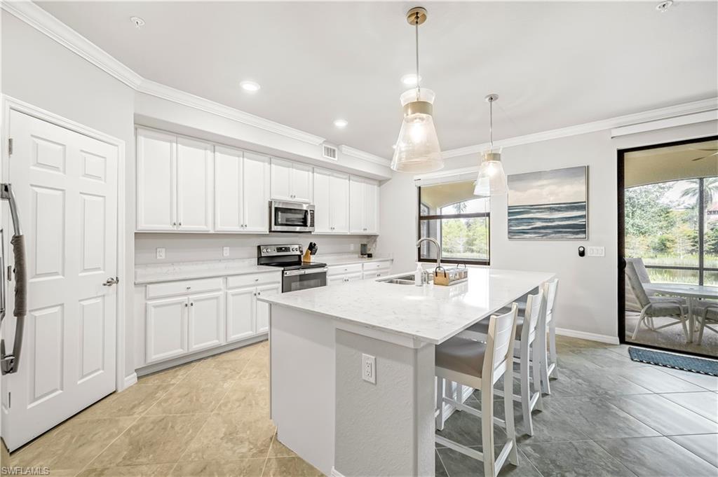 Kitchen with a kitchen breakfast bar, ornamental molding, an island with sink, appliances with stainless steel finishes, and white cabinets