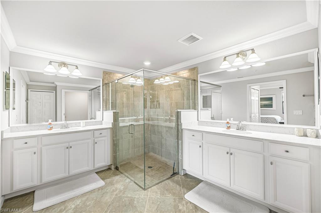 Ensuite bathroom with crown molding, a stall shower, two vanities, and light tile patterned floors