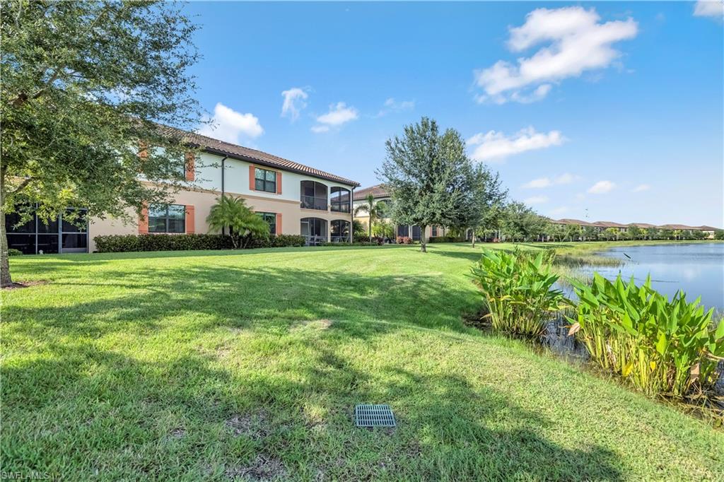 View of green lawn with a water view, a balcony, and a sunroom